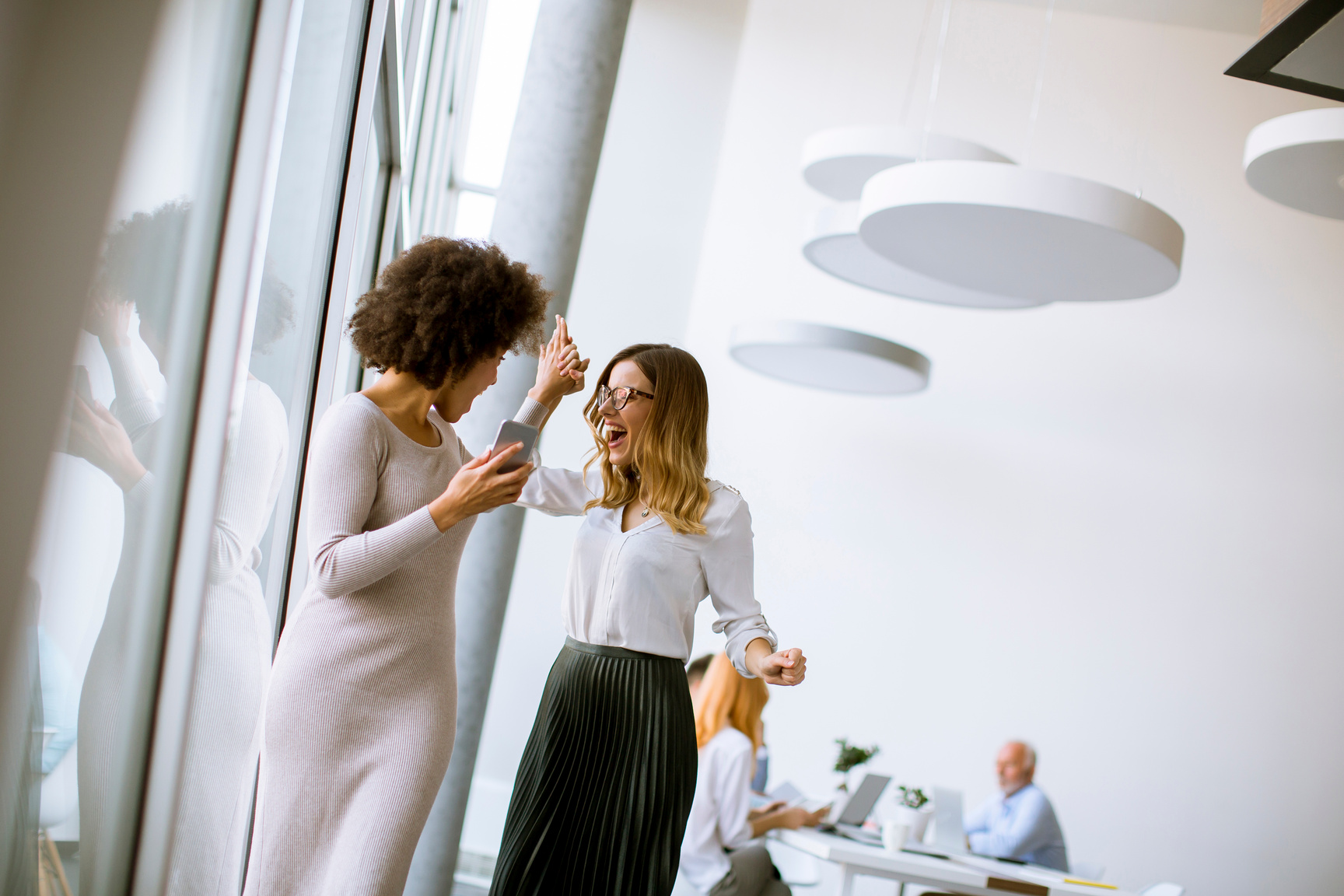 Two Young Businesswomen with a Mobile Phone in the Office